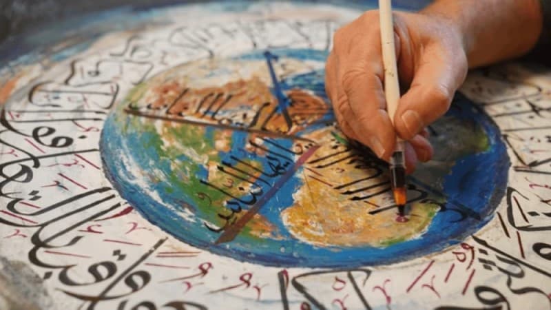 A hand writing Arabic calligraphy with a traditional reed pen